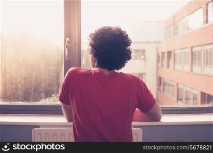 Young man is at the window silll and looking out at sunset