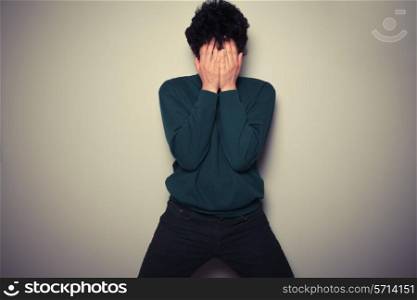Young man is hiding his face in the palms of his hands