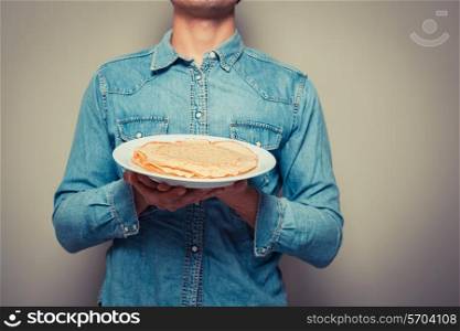 Young man is presenting a plate with a stack of pancakes