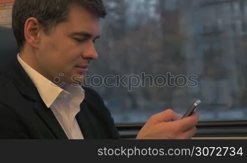 Young man is sitting in couch and using his smartphone for doing business.