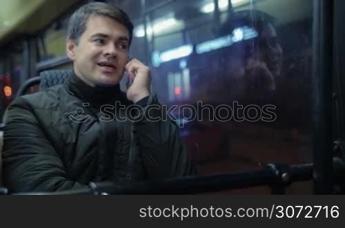 Young man is sitting in the moving bus and talking on the phone.