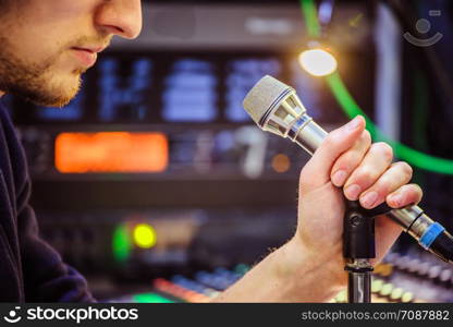 Young man is sitting in the recording studio and talks into the microphone, buttons and equipment in the blurry background