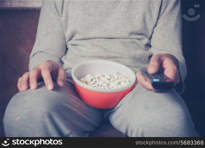 Young man is sitting on a sofa and eating popcorn while watching television