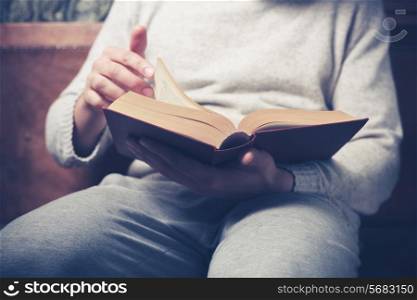 Young man is sitting on a sofa and flipping the pages of a big book