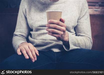 Young man is sitting on a sofa and holding a paper cup