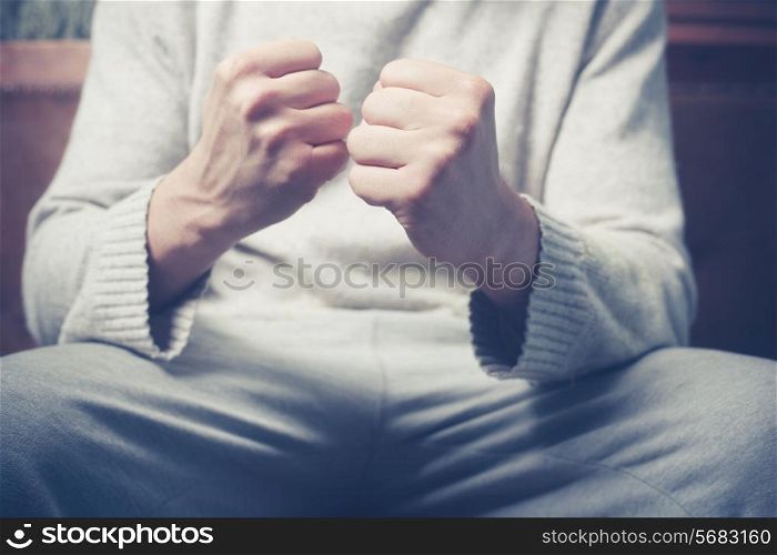 Young man is sitting on a sofa with his fists clenched