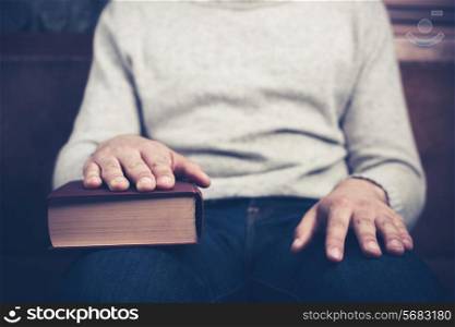 Young man is sitting on a sofa with his hand on a big book