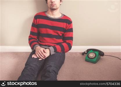 Young man is sitting on the floor with a telephone next to him