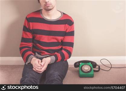Young man is sitting on the floor with an old rotary telephone