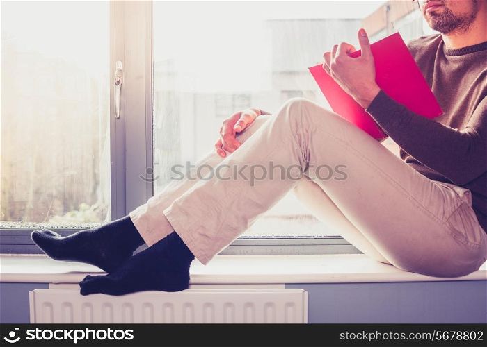 Young man is sitting on window sill and reading