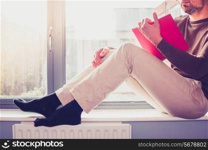 Young man is sitting on window sill and reading