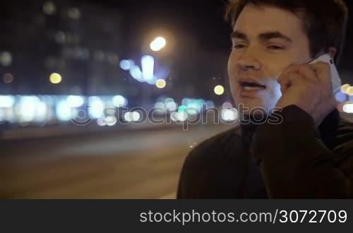 Young man is talking on the phone outdoor. Road traffic is on the background.