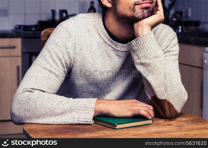 Young man is with book is sitting in kitchen