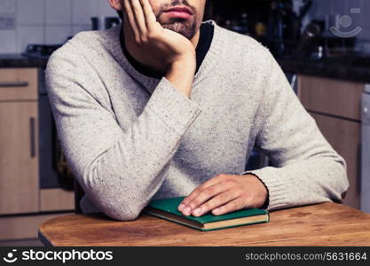 Young man is with book is sitting in kitchen