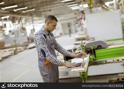 Young man is working on laptop at the furniture factory
