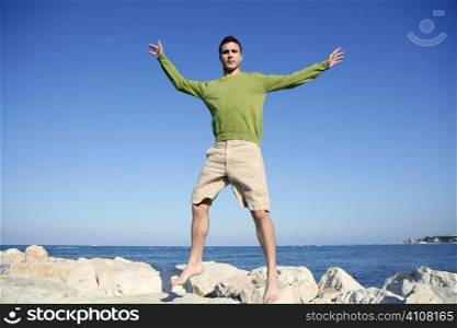 Young man jump over stones in ocean blue shore, sunny summer day