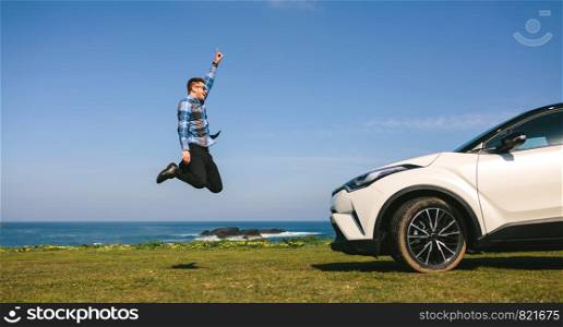 Young man jumping happy in front of a car outdoors. Young man jumping happy with car