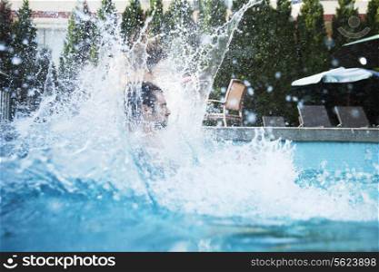 Young man jumping into a pool with water splashing all around him