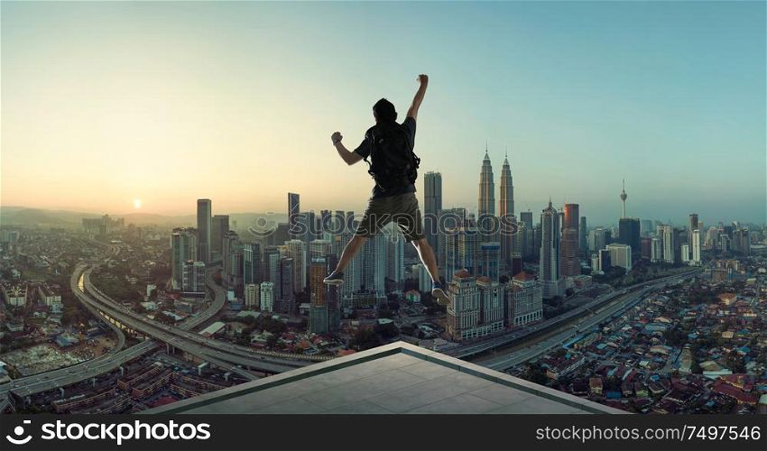 Young man jumping on rooftop with great cityscape sunrise view.