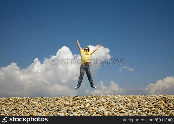 young man jumps on beach, with the sky as background