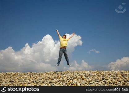 young man jumps on beach, with the sky as background