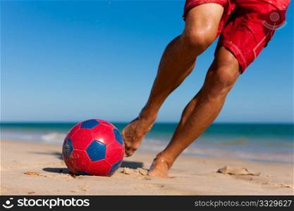 Young man (just feet) on the beach playing soccer in his vacation, he is about to kick the ball