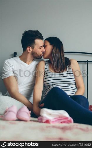 Young man kissing his pregnant wife in the bedroom. Man kissing his pregnant wife