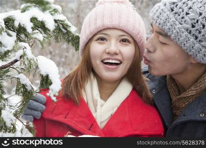 Young man kissing young woman in park in snow