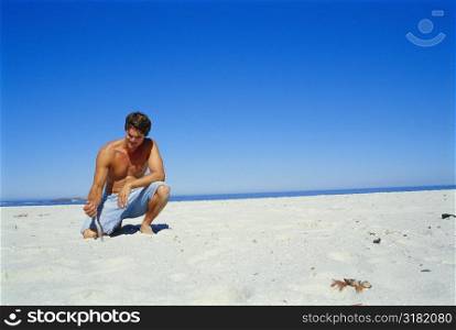 Young man kneeling in sand on the beach