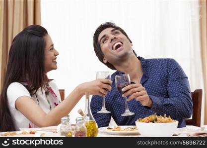 Young man laughing while having wine with his girlfriend at restaurant