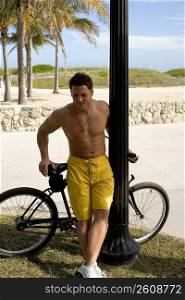 Young man leaning against bicycle at beach
