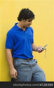 Young man leaning against the wall and using a mobile phone