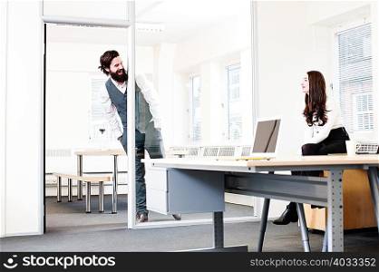 Young man leaning into office talking to woman