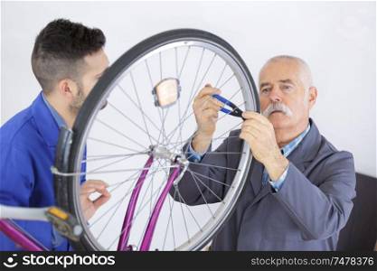 young man learning how to repair bicycle wheel with mentor
