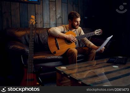 Young man learning play guitar at home reading musical notes. Online lesson, distance education. Young man learning play guitar at home