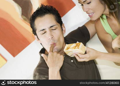 Young man licking his finger with a young woman holding a pastry