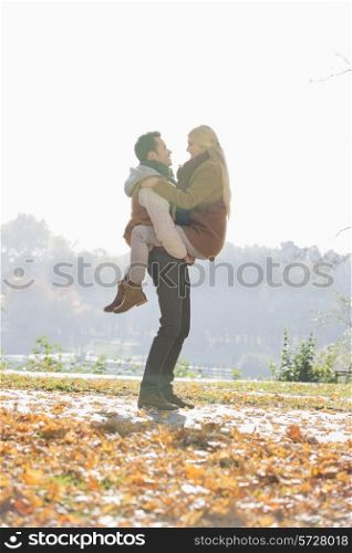Young man lifting woman in park during autumn