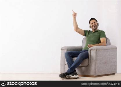 Young man listening music on headphones and having fun while sitting on sofa