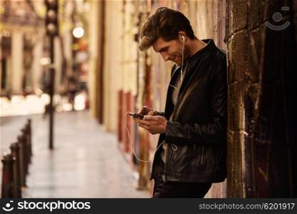 Young man listening music with smartphone earphones in the street