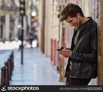 Young man listening music with smartphone earphones in the street