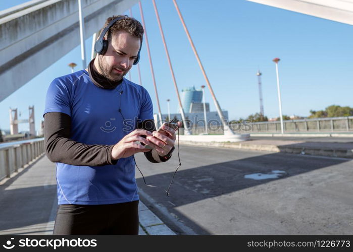 young man looking at his cell phone to listen to music while running through an urban area