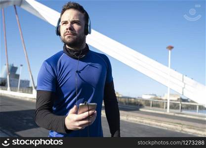 young man looking at his cell phone to listen to music while running through an urban area