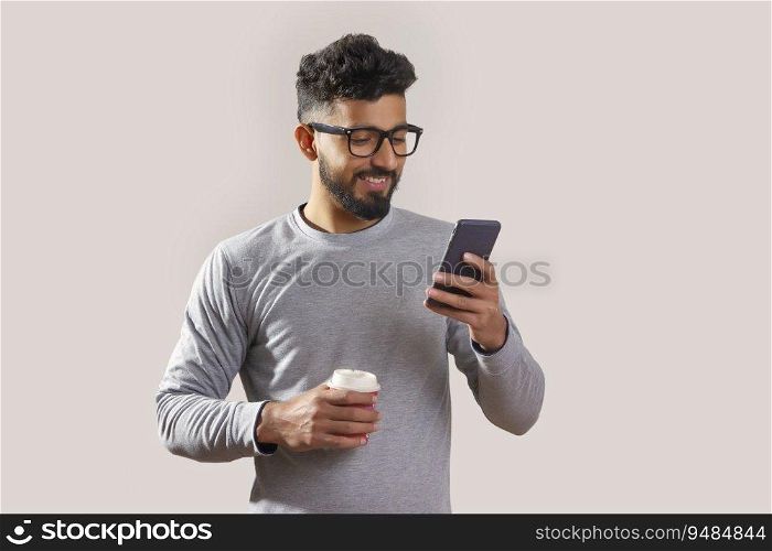 Young man looking at his phone and holding a coffee cup. 