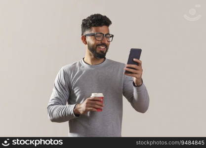 Young man looking at his phone and holding a coffee cup. 