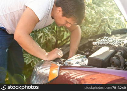 Young man looking at open car hood and fixing engine