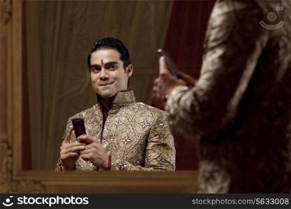 Young man looking at self in mirror and smiling while holding mobile phone