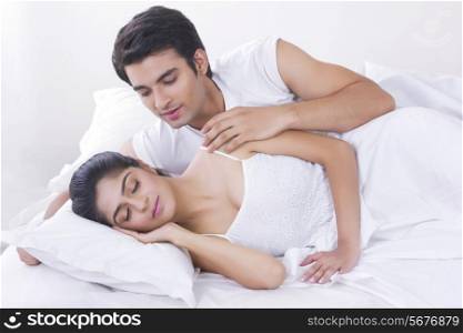 Young man looking at woman sleeping in bed