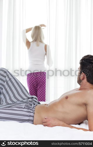 Young man looking at woman standing by window in hotel room