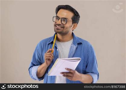 Young man looking away and thinking with pencil and notebook in his hand