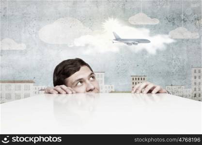 Young man looking from under table on flying airplane. No limits for communication